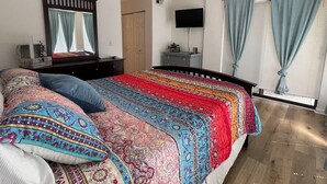Une chambre à coucher avec un grand lit, un ventilateur de plafond, une télévision et une fenêtre avec des rideaux.