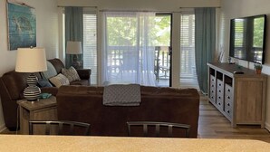 Un salon avec un canapé marron, une table basse, un meuble pour la télévision et un coin repas comprenant une table et des chaises.