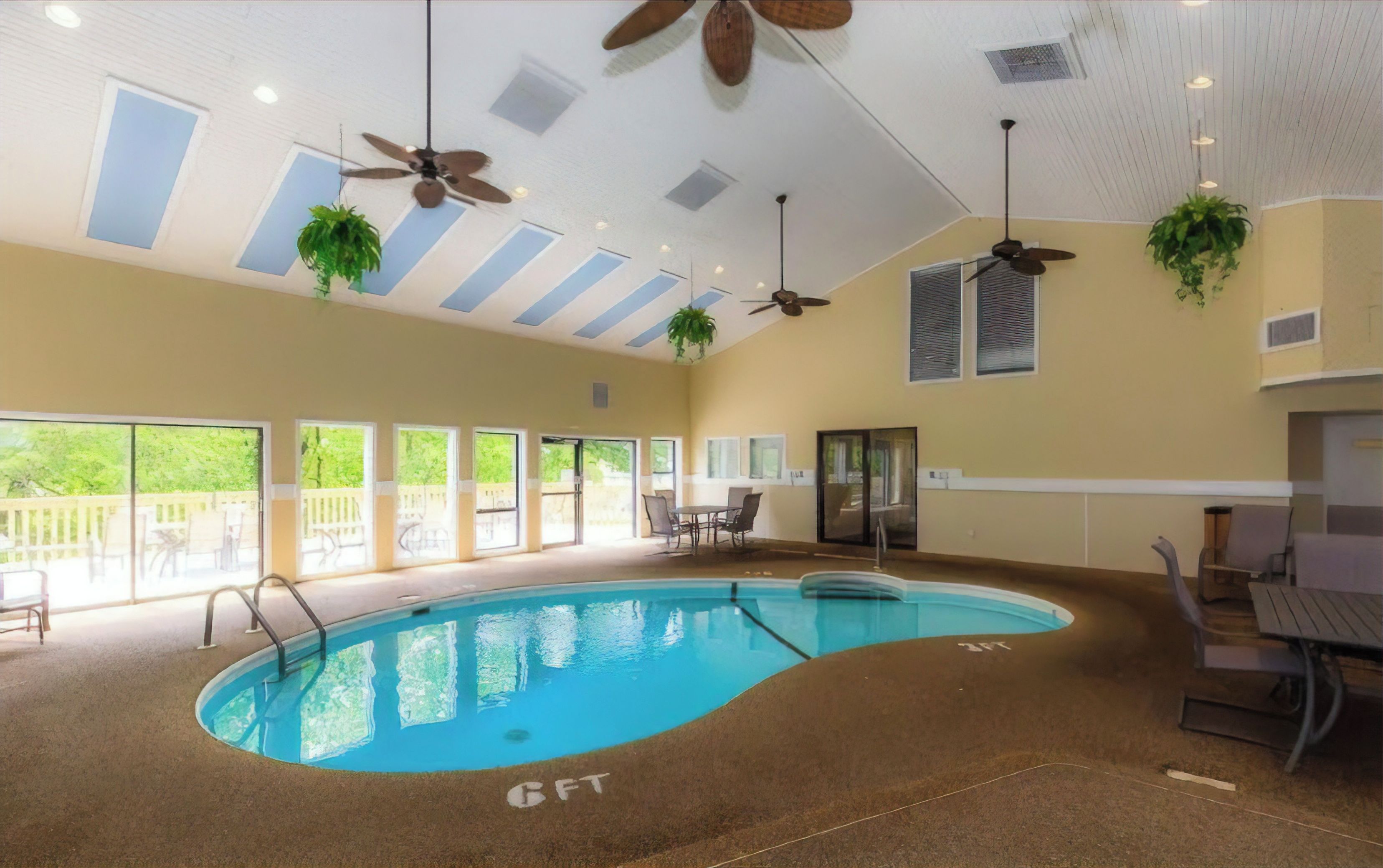 An indoor swimming pool with ceiling fans, large windows, and outdoor seating.