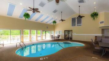 An indoor swimming pool with ceiling fans, large windows, and outdoor seating.