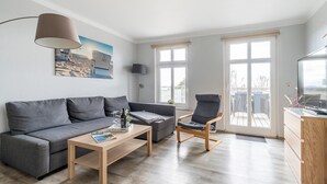 A modern living room with a grey sofa, a wooden coffee table, a grey armchair, and a TV stand. - Apartment 05 - house holiday happiness (Sellin)