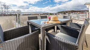 An outdoor patio with wicker furniture and a glass table, overlooking a scenic landscape. - Apartment 05 - house holiday happiness (Sellin)