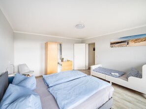 Une chambre à coucher moderne avec un lit, un canapé, une commode et un tableau représentant une scène de plage.