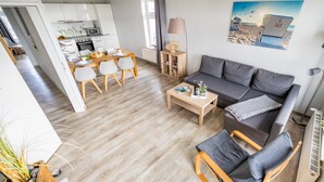 A modern living room with a grey sofa, wooden coffee table, and a dining area with a wooden table and chairs. - Apartment 05 - house holiday happiness (Sellin)
