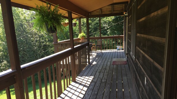 Een houten terras met een leuning, plantenpotten en uitzicht op groen.