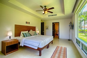 A bedroom with a bed, nightstands, a ceiling fan, a window with a view, and a door leading to another room. - Beachfront 2BR | Accessible, Pool & Hot Tub (Puerto Vallarta)