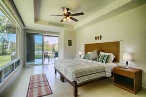 A bedroom with a bed, nightstands, a ceiling fan, and a view through a sliding glass door to a patio. - Beachfront 2BR | Accessible, Pool & Hot Tub (Puerto Vallarta)