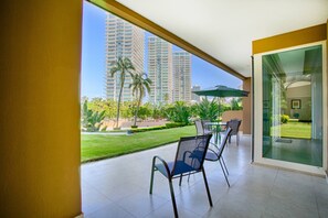 Une chambre d’hôtel moderne avec un balcon donnant sur un jardin bien entretenu et des immeubles de grande hauteur.