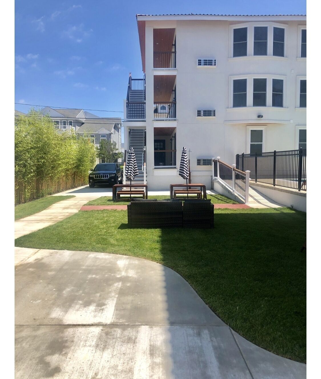 A residential building with a front yard, a driveway, and a black car parked on the street.
