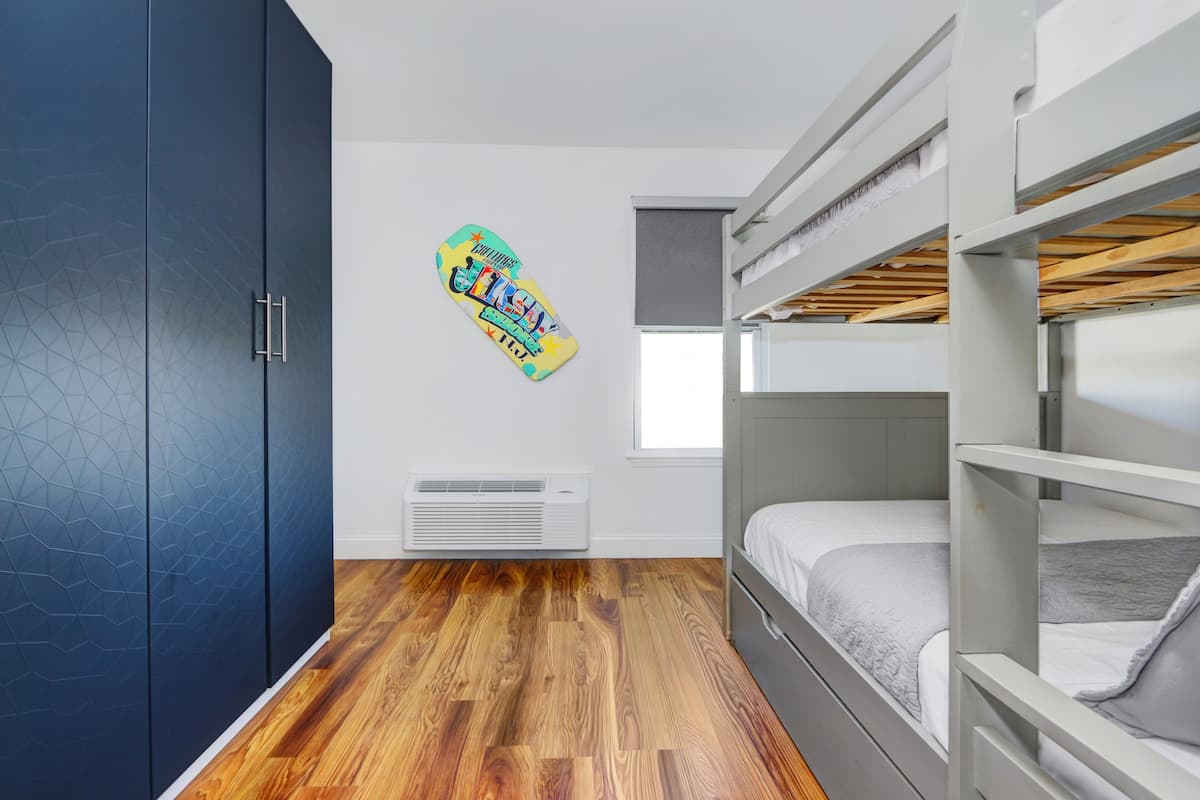 A modern bedroom with a bunk bed, a geometric-patterned wardrobe, and a skateboard on the wall.