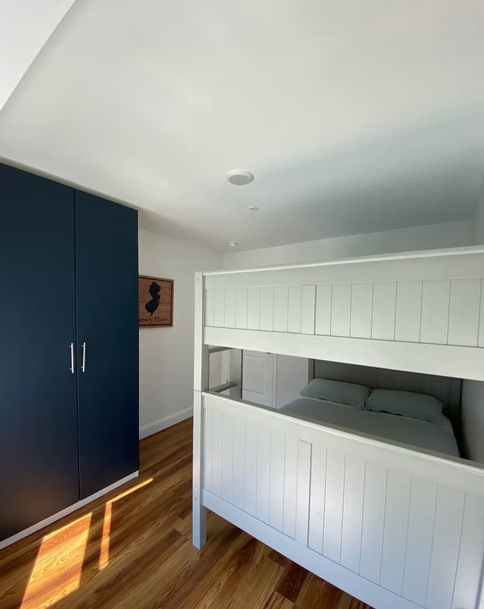 A room with a bunk bed, a dark blue wardrobe, and a framed picture on the wall.