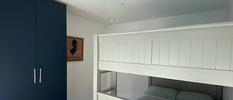 A room with a bunk bed, a dark blue wardrobe, and a framed picture on the wall.