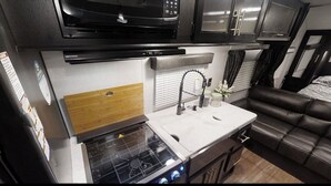 Una kitchenette compacta equipada con microondas, estufa y un salpicadero de madera.