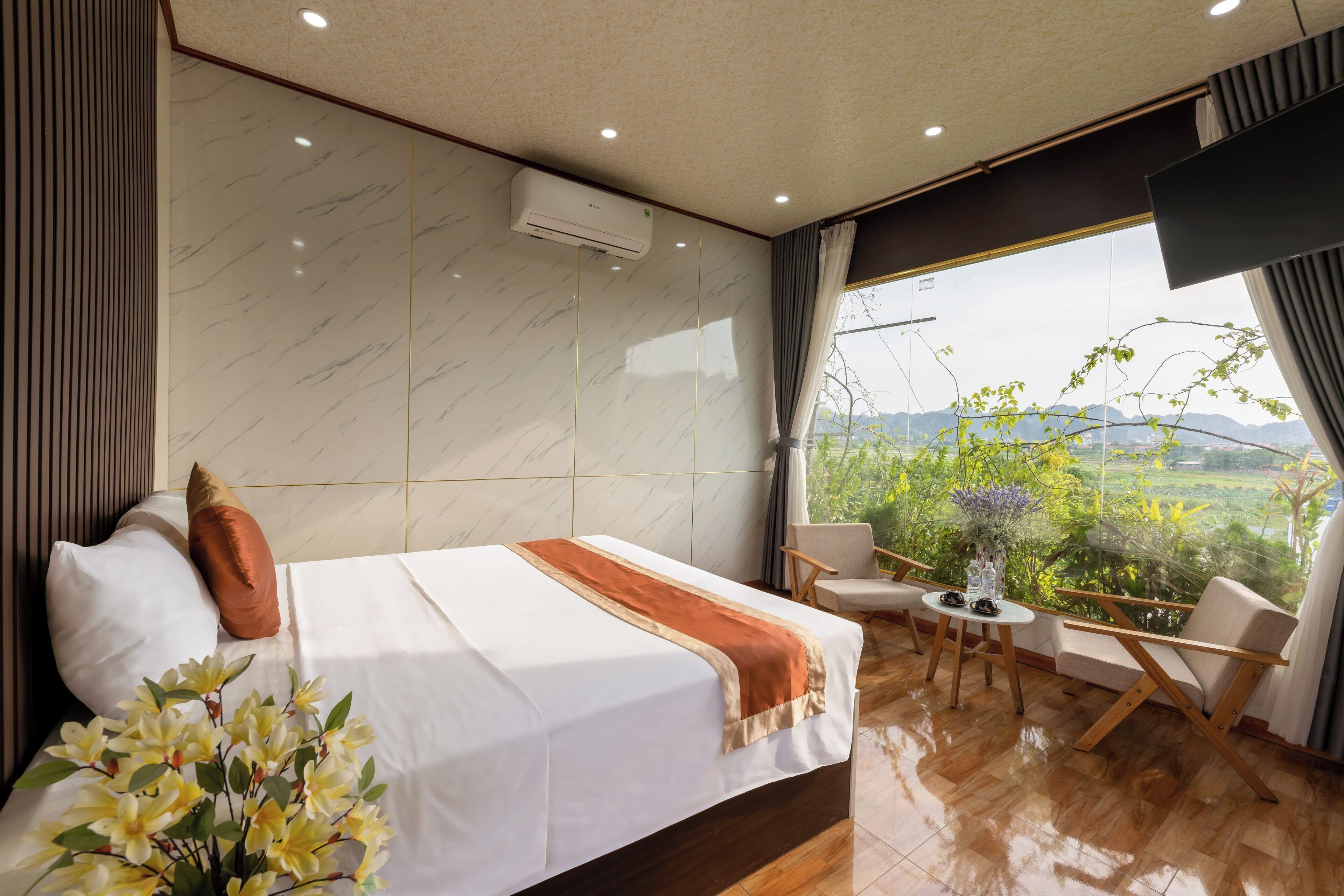 A modern hotel room with a large bed, a small table, and a view of greenery.