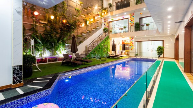 Piscina interior com barreira de vidro, rodeada por um espaço coberto por carpete verde e espreguiçadeiras.