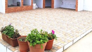 Un espace cuisine extérieur en briques, doté d’une cheminée et entouré de plantes en pot.