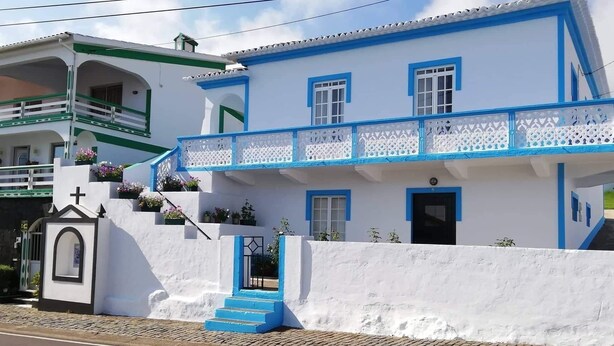 Un bâtiment blanc agrémenté de touches de bleu et une petite structure ressemblant à une chapelle, surmontée d’une croix.