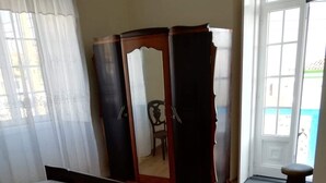 Une chambre à coucher comprenant un lit, une armoire, une chaise et une vue sur l’extérieur par une fenêtre.