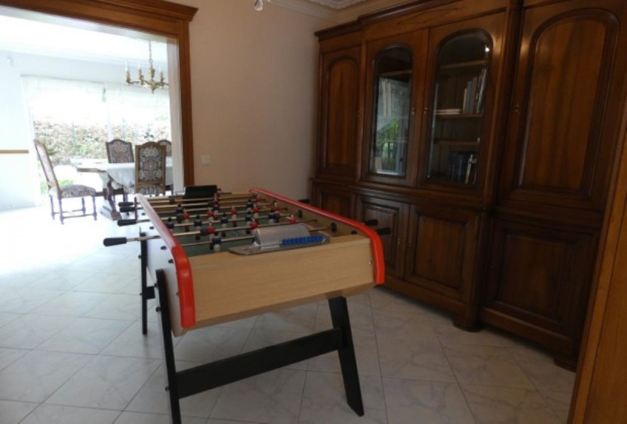 A foosball table in a room with a large wooden cabinet and a dining area visible through an open door.