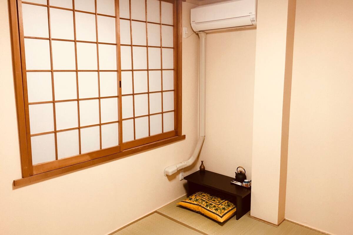 Une pièce avec un tatami, une petite table sur laquelle se trouve une bouilloire, et une fenêtre à carreaux.