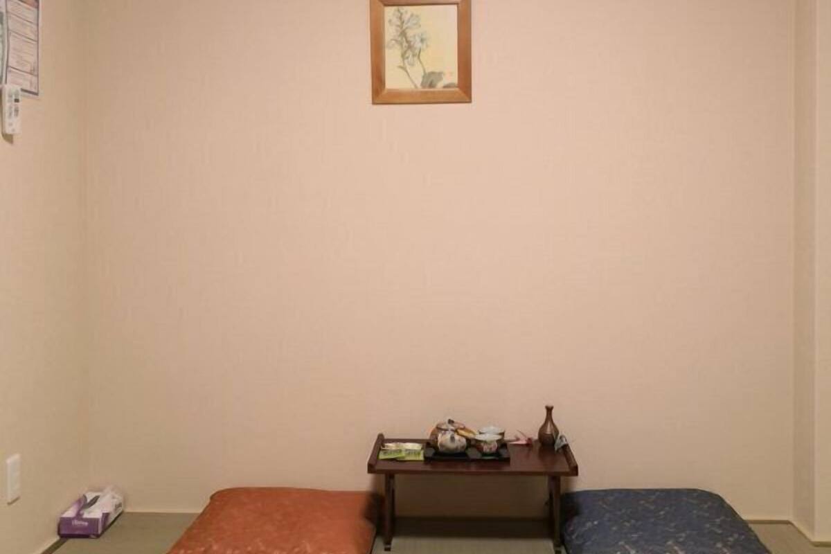 Une pièce avec des tatamis, une petite table sur laquelle se trouve une théière et un tableau encadré accroché au mur.