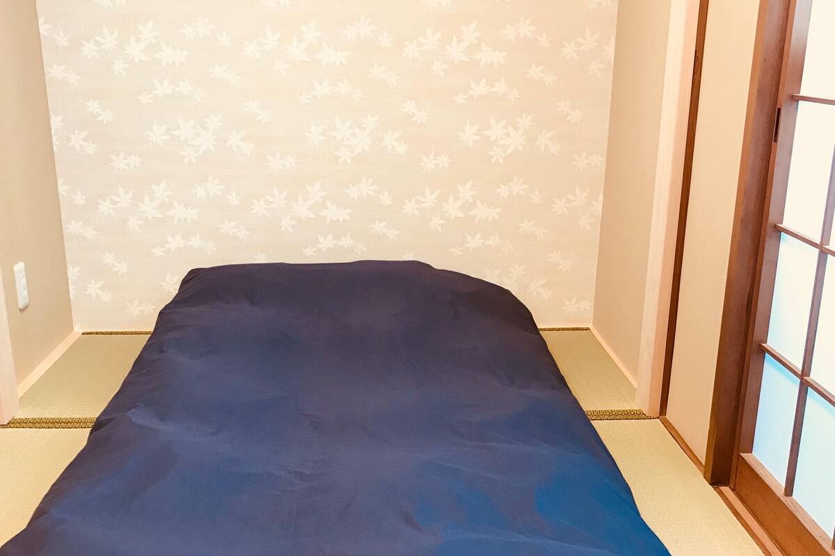 Une petite pièce avec un lit simple, un papier peint à motifs et une porte coulissante.