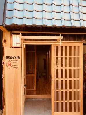Une maison d’hôtes japonaise traditionnelle, avec une façade en bois, un toit recouvert de tuiles et une porte coulissante.