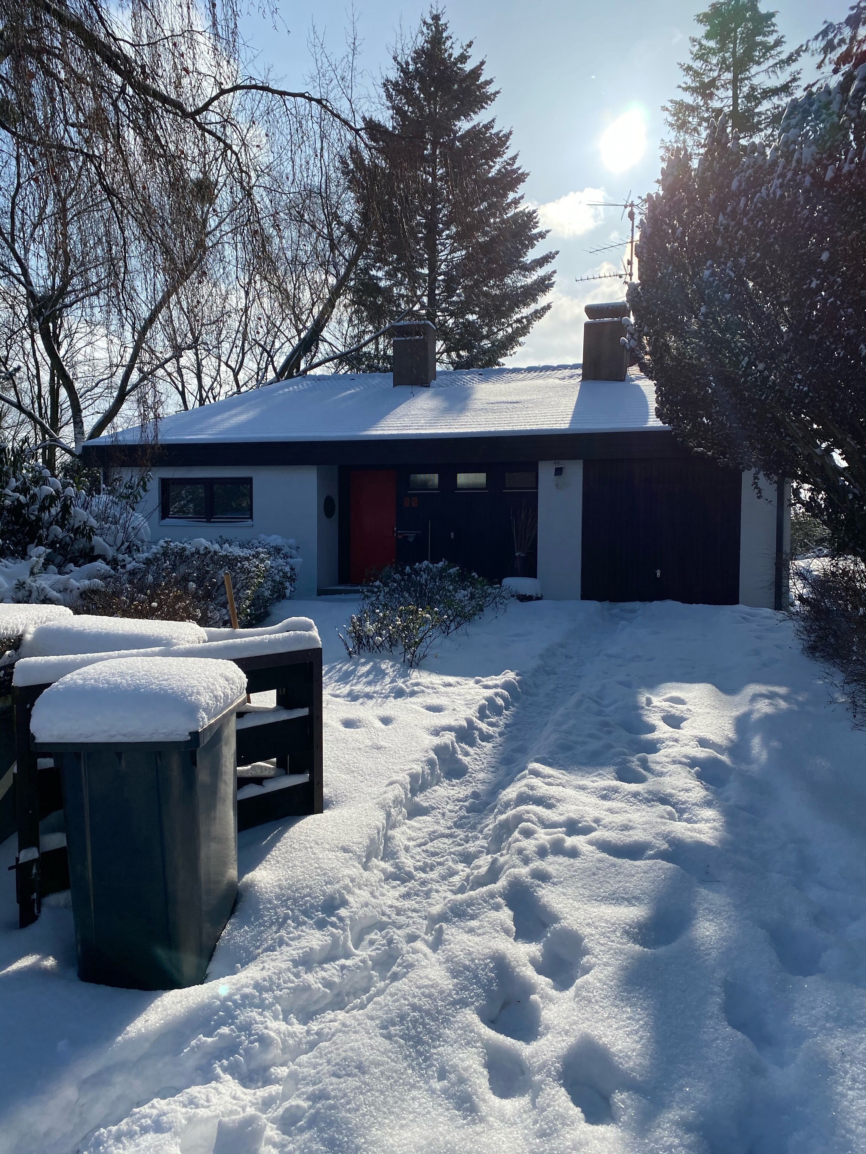 Ein modernes Haus mit verschneitem Einfahrt und roter Tür.