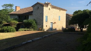 A stone building with a tiled roof, a small door, and blue shutters.