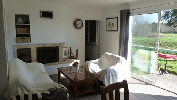 A living room with a fireplace, a dining table with chairs, a sofa, and a view of a garden through a sliding glass door. - HOUSE BETWEEN COUNTRYSIDE AND SEA (Saint-Julien-en-Born)
