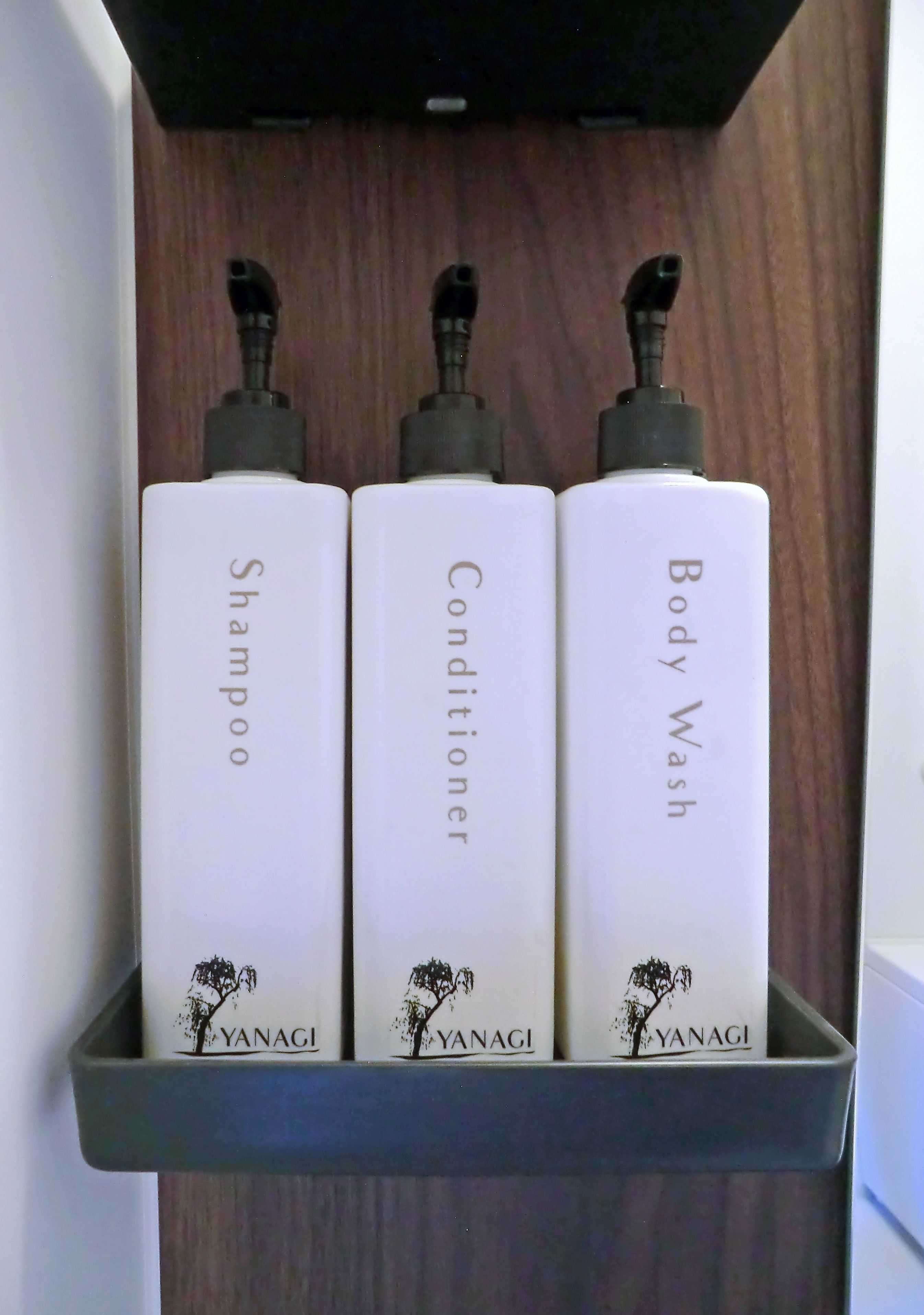 A shelf with three white bottles labeled 'Shampoo,' 'Conditioner,' and 'Body Wash' from the brand 'YANAGI.'