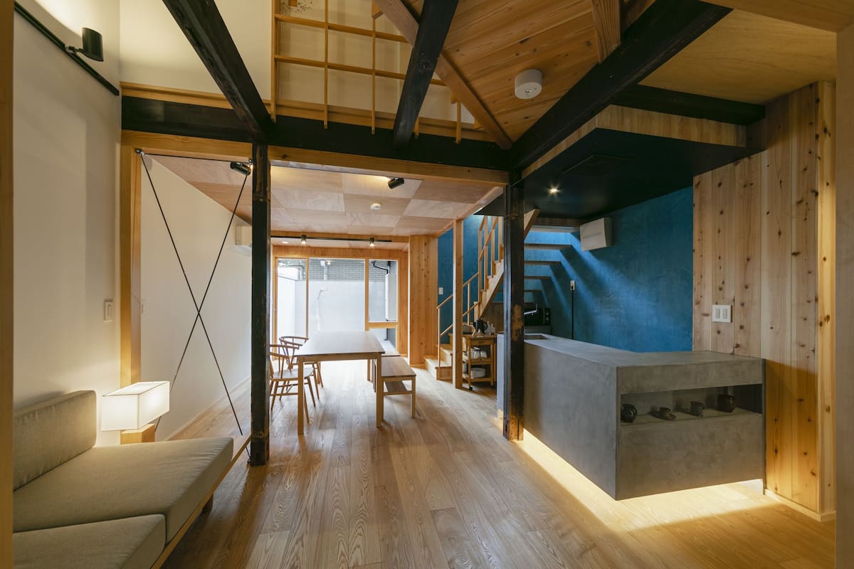 Une pièce spacieuse avec un plancher en bois, un canapé, une table à manger et un coin cuisine doté d’un comptoir.