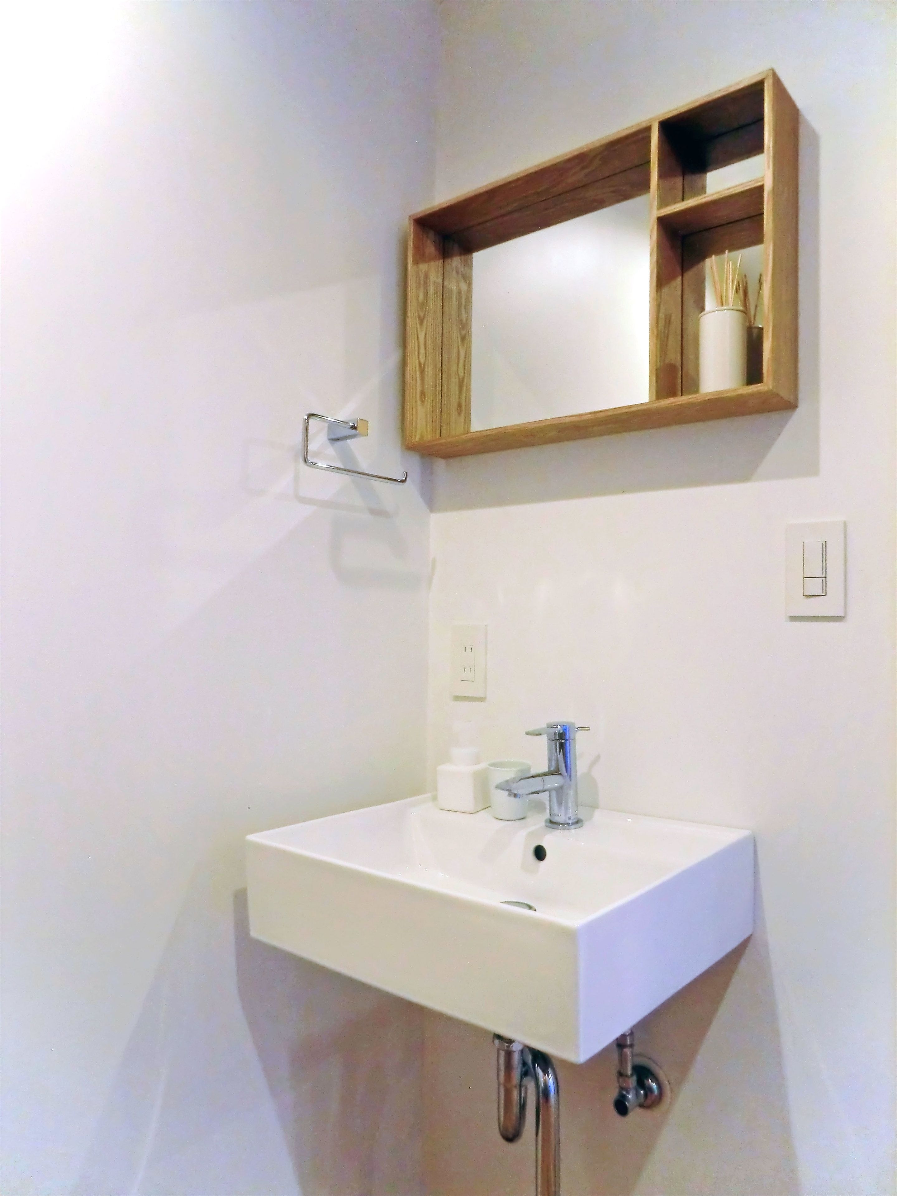 A bathroom with a white sink, a mirror, and a wooden shelf above it.