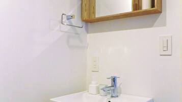 A bathroom with a white sink, a mirror, and a wooden shelf above it.