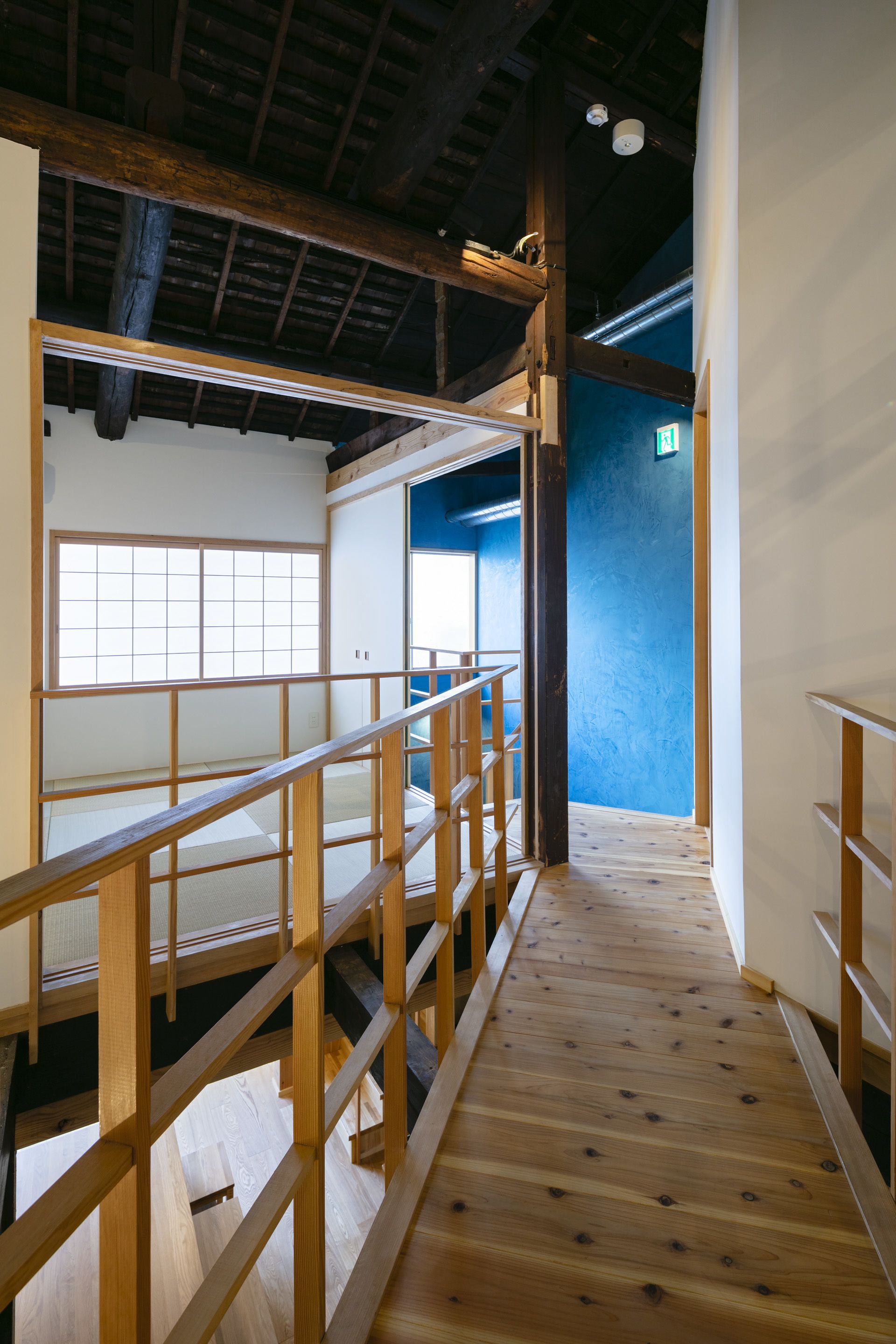 A wooden staircase with a handrail leading to a room with a large window and a blue wall.