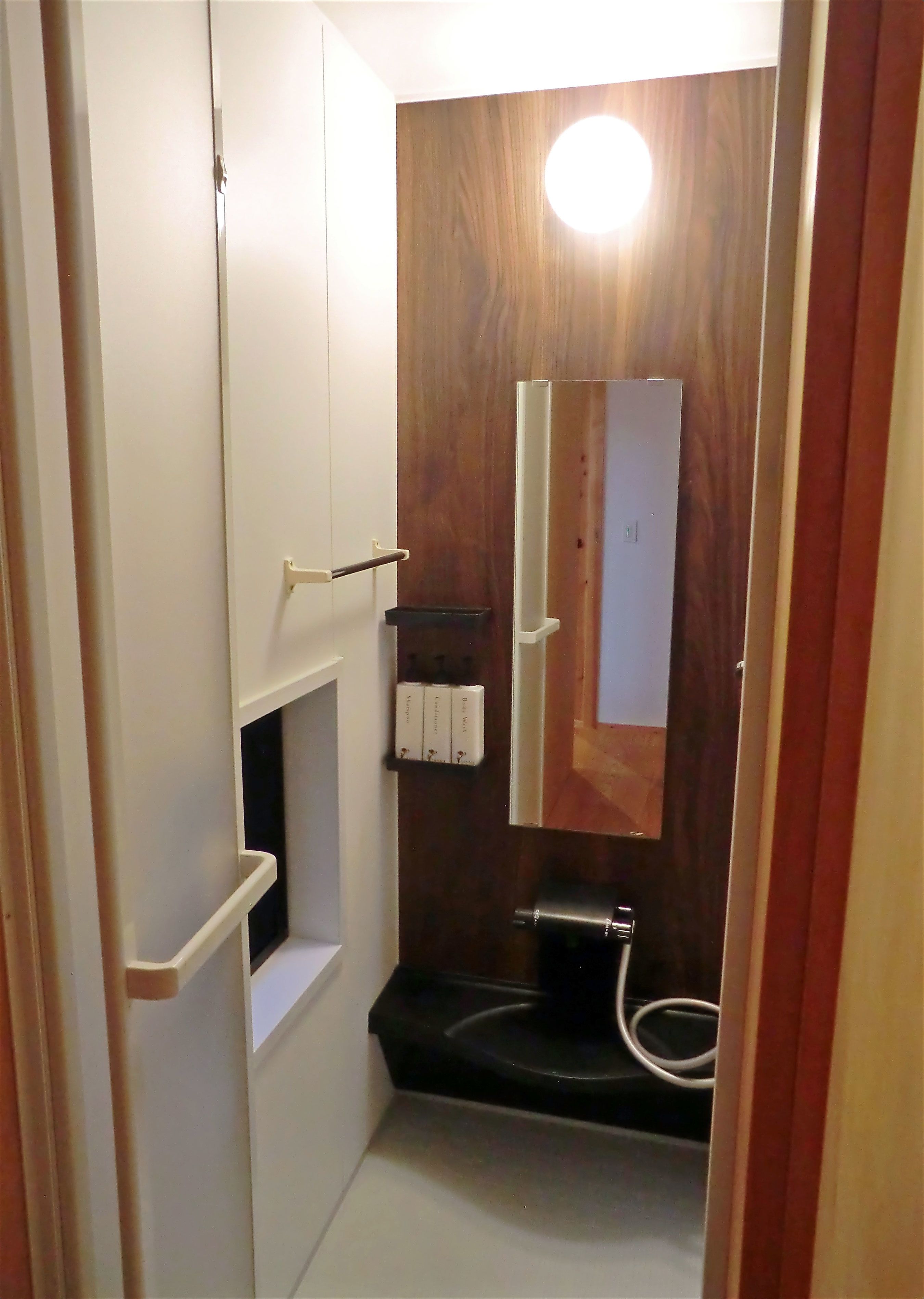 Un baño pequeño con tocador de madera, inodoro blanco y una pequeña repisa con artículos de aseo.