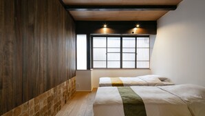 Une chambre avec deux lits, un plancher en bois, un mur carrelé et une fenêtre avec des stores.