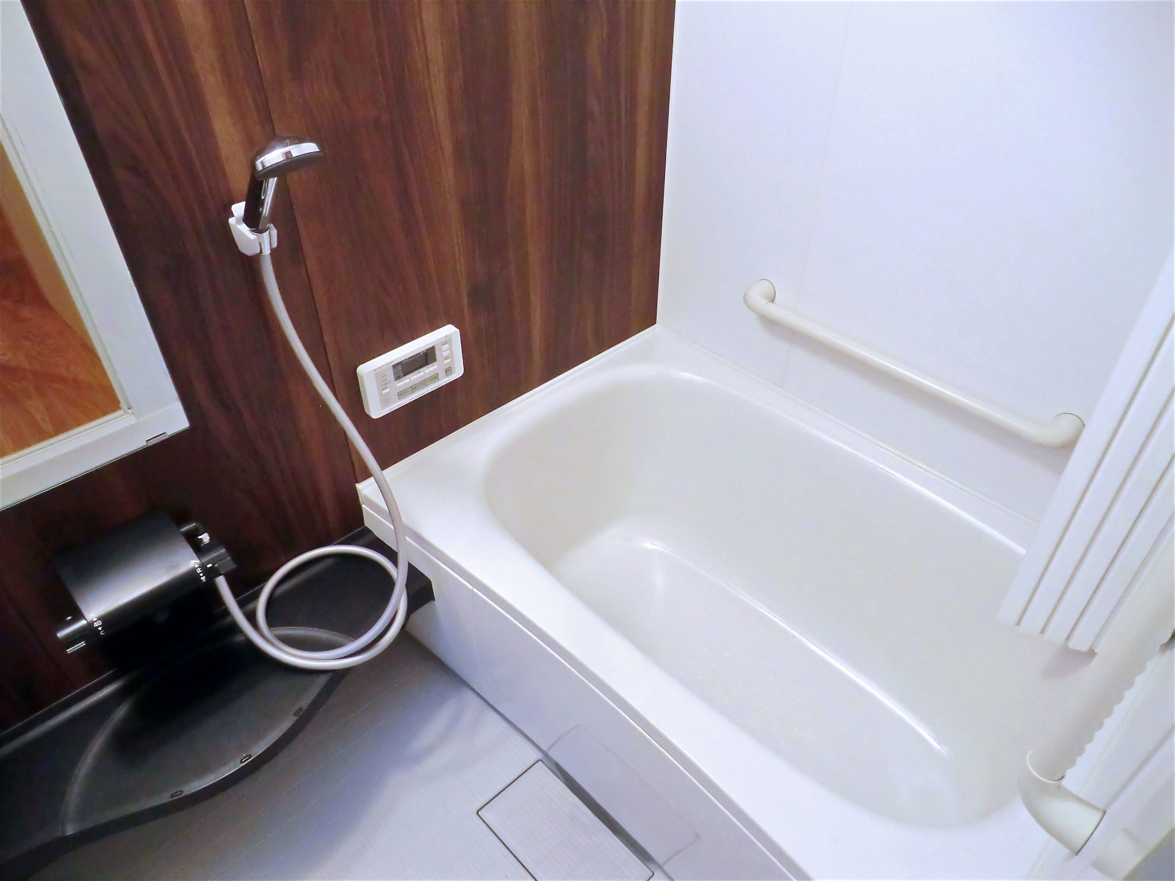 Un baño con una bañera blanca, un cabezal de ducha de mano y un inodoro blanco.
