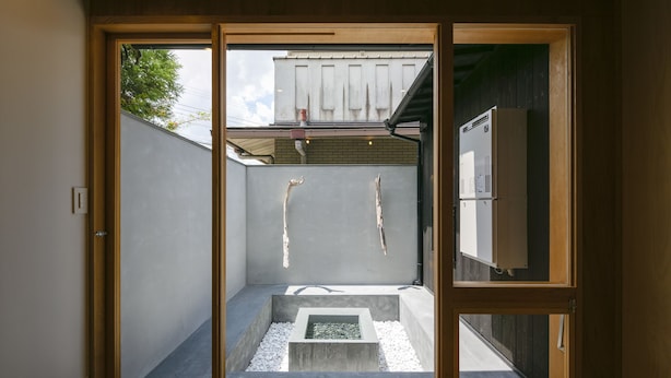 Un intérieur moderne avec une porte-fenêtre coulissante donnant sur un espace extérieur doté d’une structure en béton et d’un petit élément décoratif aquatique.