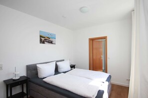 Une chambre à coucher avec un lit, deux tables de chevet, une commode, un tableau au mur et une porte.