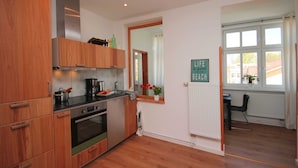 A modern kitchen with wooden cabinets, stainless steel appliances, and a window with a view of buildings. - 02: 66 m², 3-room, 4 pers., Veranda, garden, wifi - Villa Elise (Göhren)