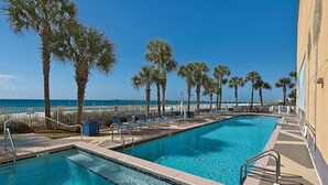 Une piscine avec des chaises longues et des palmiers, donnant sur une plage.