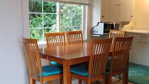 Een eetruimte met een houten tafel en stoelen, een raam met uitzicht op groen en een magnetron op het aanrecht.