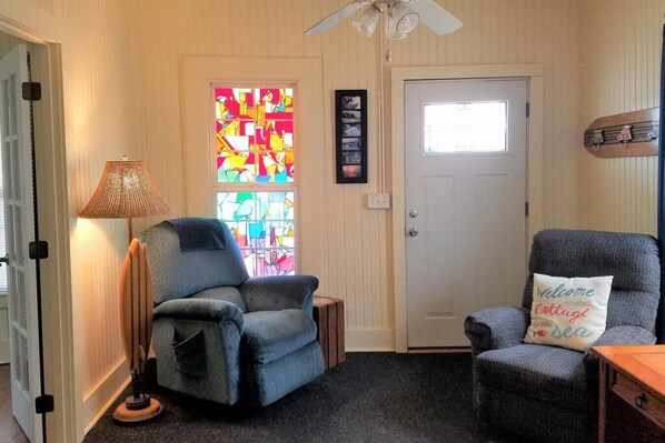 A cozy room with a blue armchair, a lamp, a stained glass window, and a door with a small window.