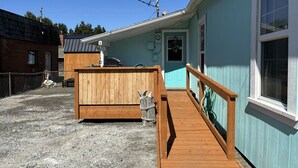 Een houten terras dat leidt naar een gebouw met een lichtblauwe gevel en een klein terras.