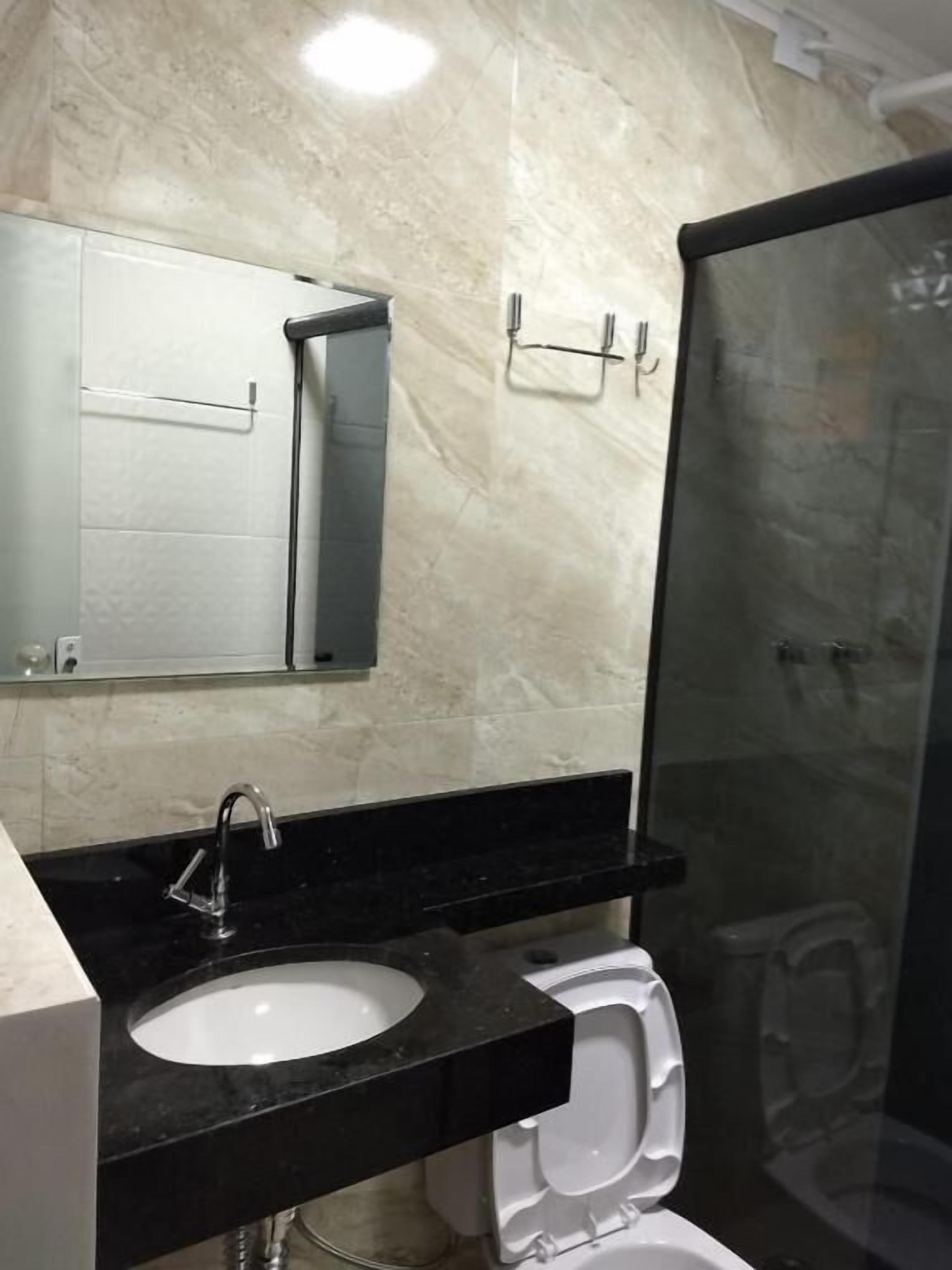 A bathroom with a black countertop, a white sink, a mirror, and a toilet.