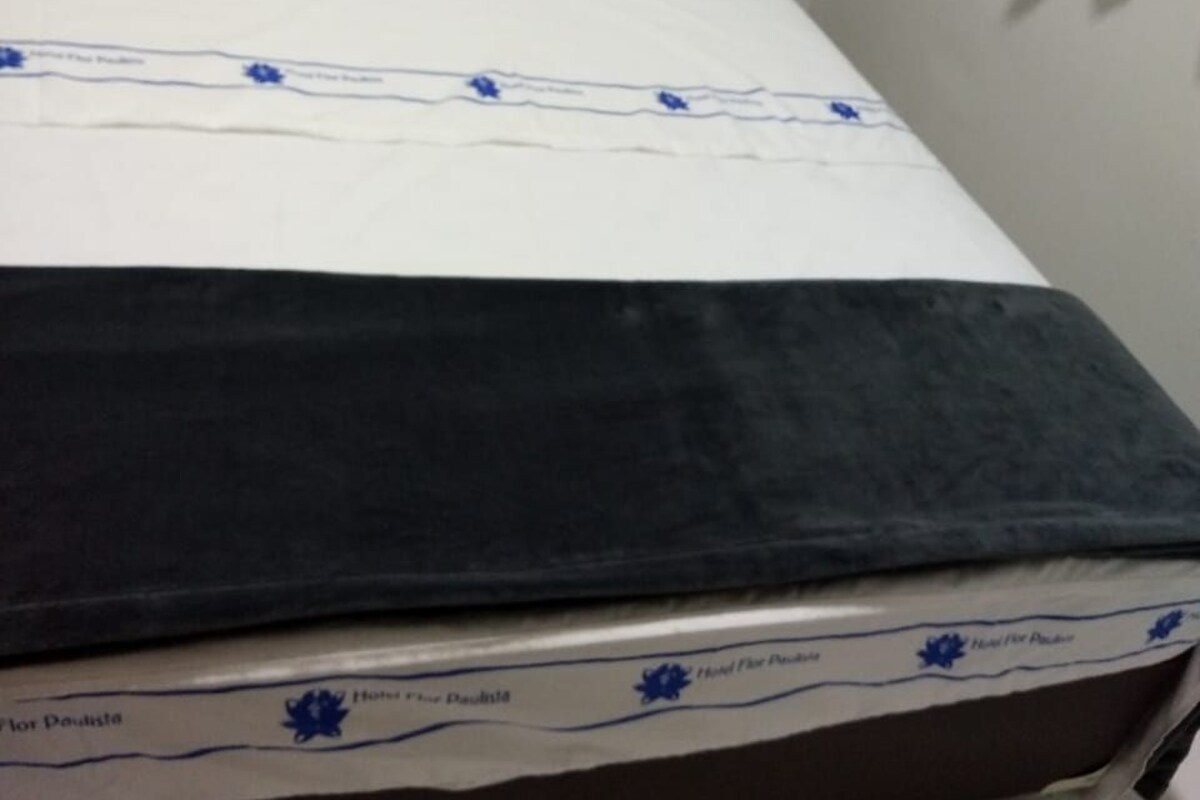 A bed with white bedding and a dark blue blanket, a white pillow, and a blue logo on the bedspread.