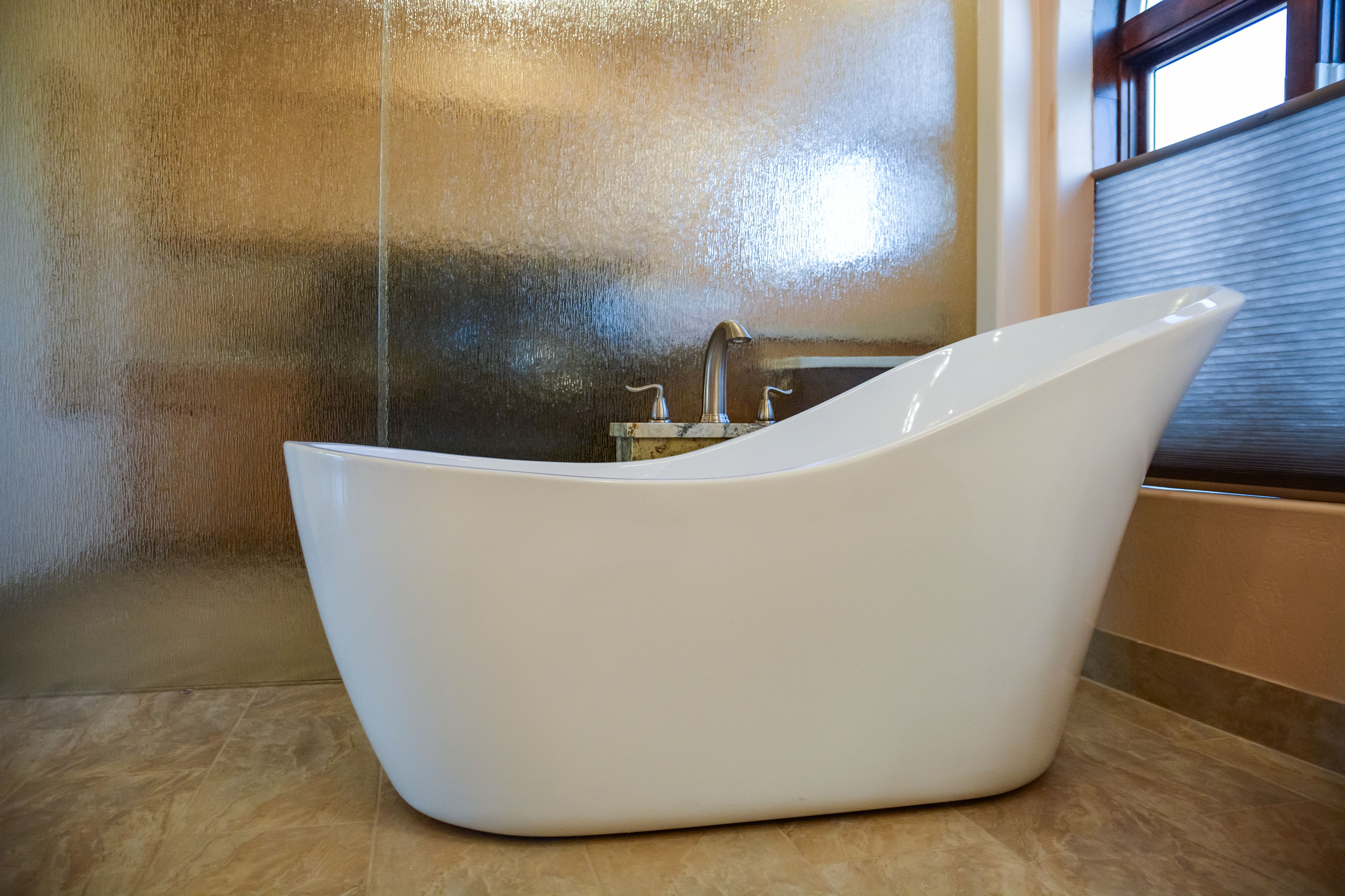 A modern bathroom with a freestanding bathtub, a glass shower enclosure, and a window providing natural light.