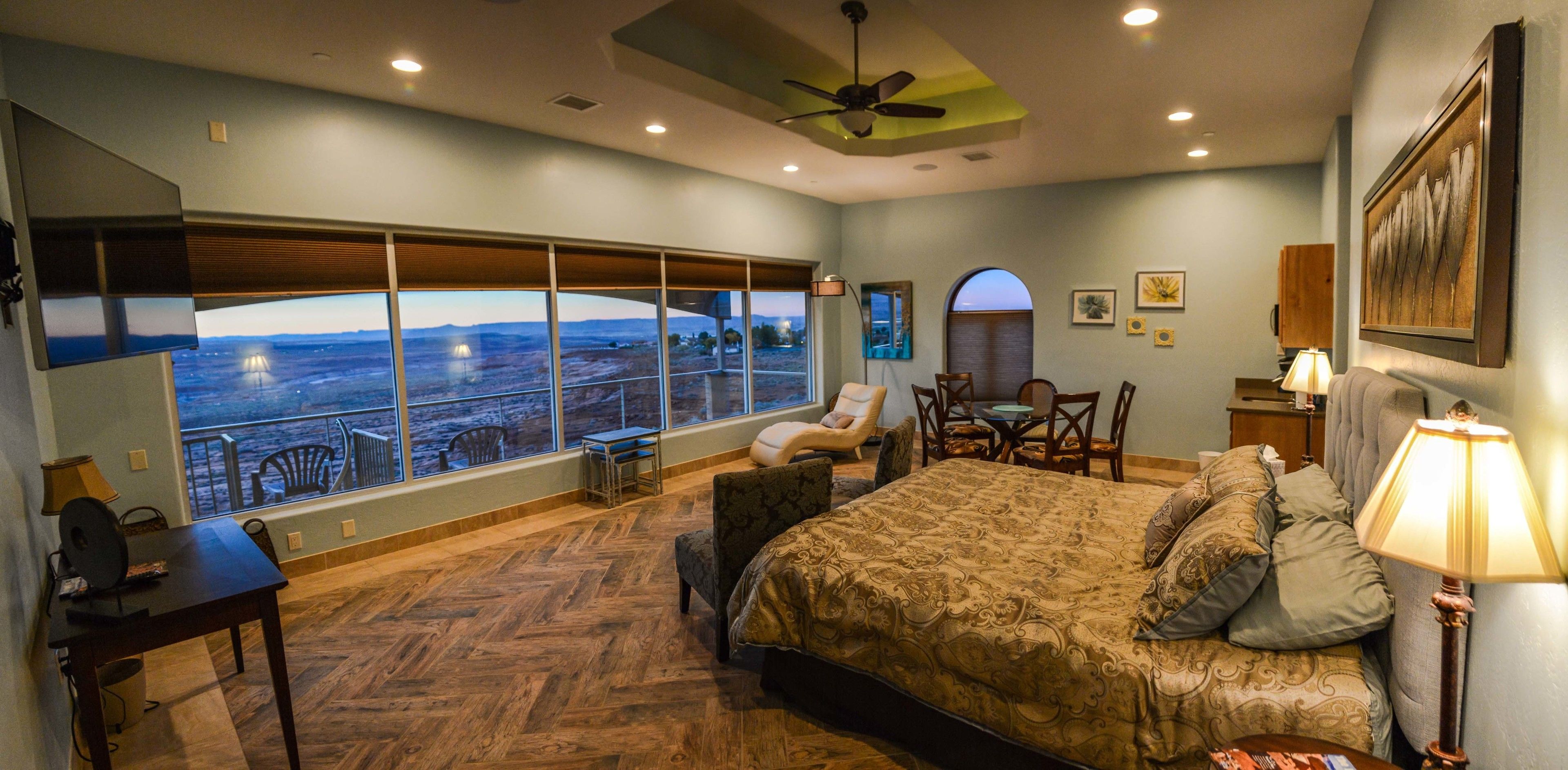 A bedroom with a large window, a bed, a desk, and a chair.