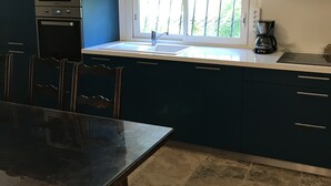 A kitchen with dark blue cabinets, a built-in oven, a window with a view of greenery, and a hanging pot rack. - St RAPHAEL 400m from the beach 2 bedrooms sleeps 6 (Saint-Raphaël)